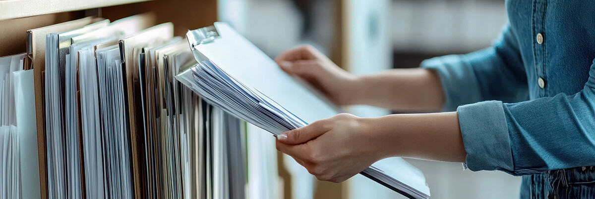 Person holding files next to shelf of many other files