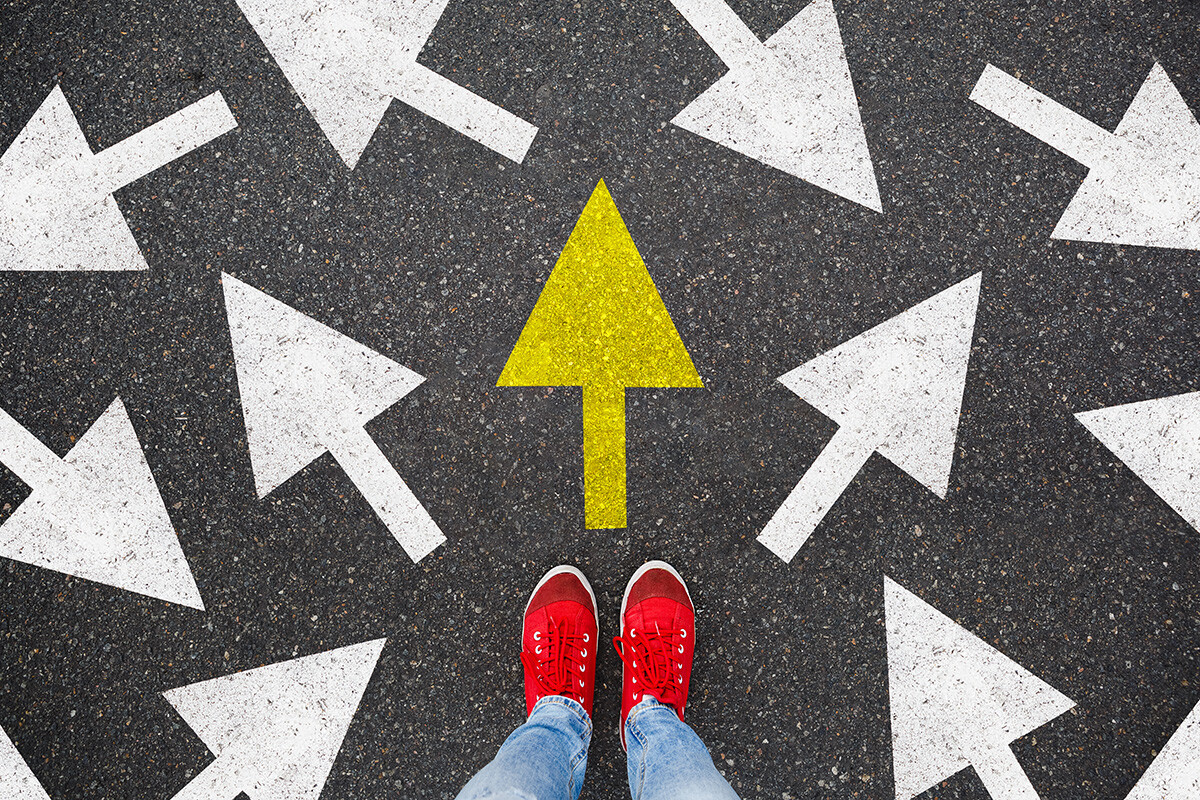 Person standing amongst arrows pointing different directions, with one in yellow pointing straight ahead 