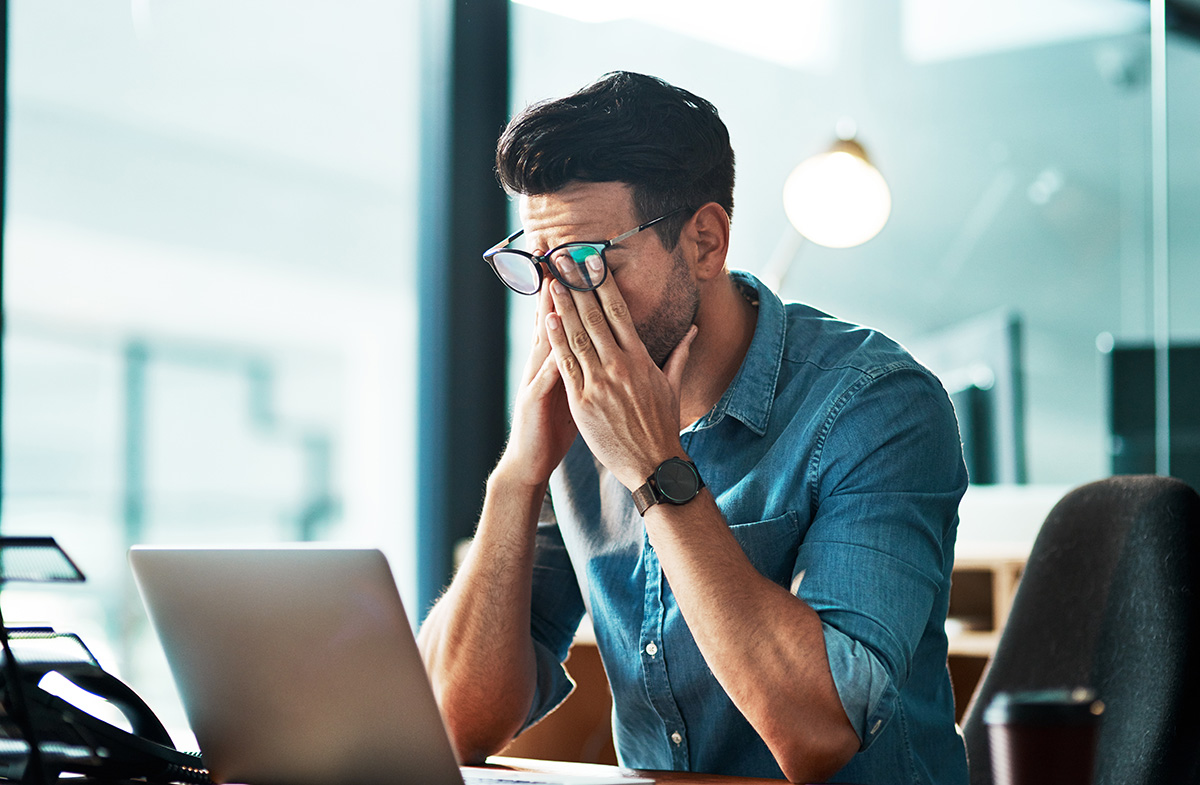 Man stressfully rubbing face while working at laptop