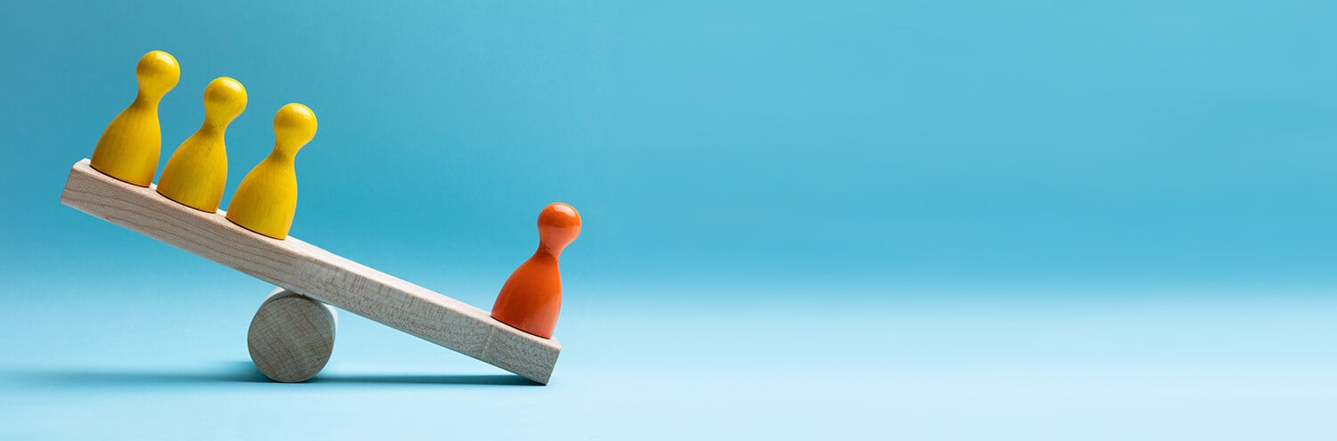 Red and yellow pawn figures balancing on wooden seesaw